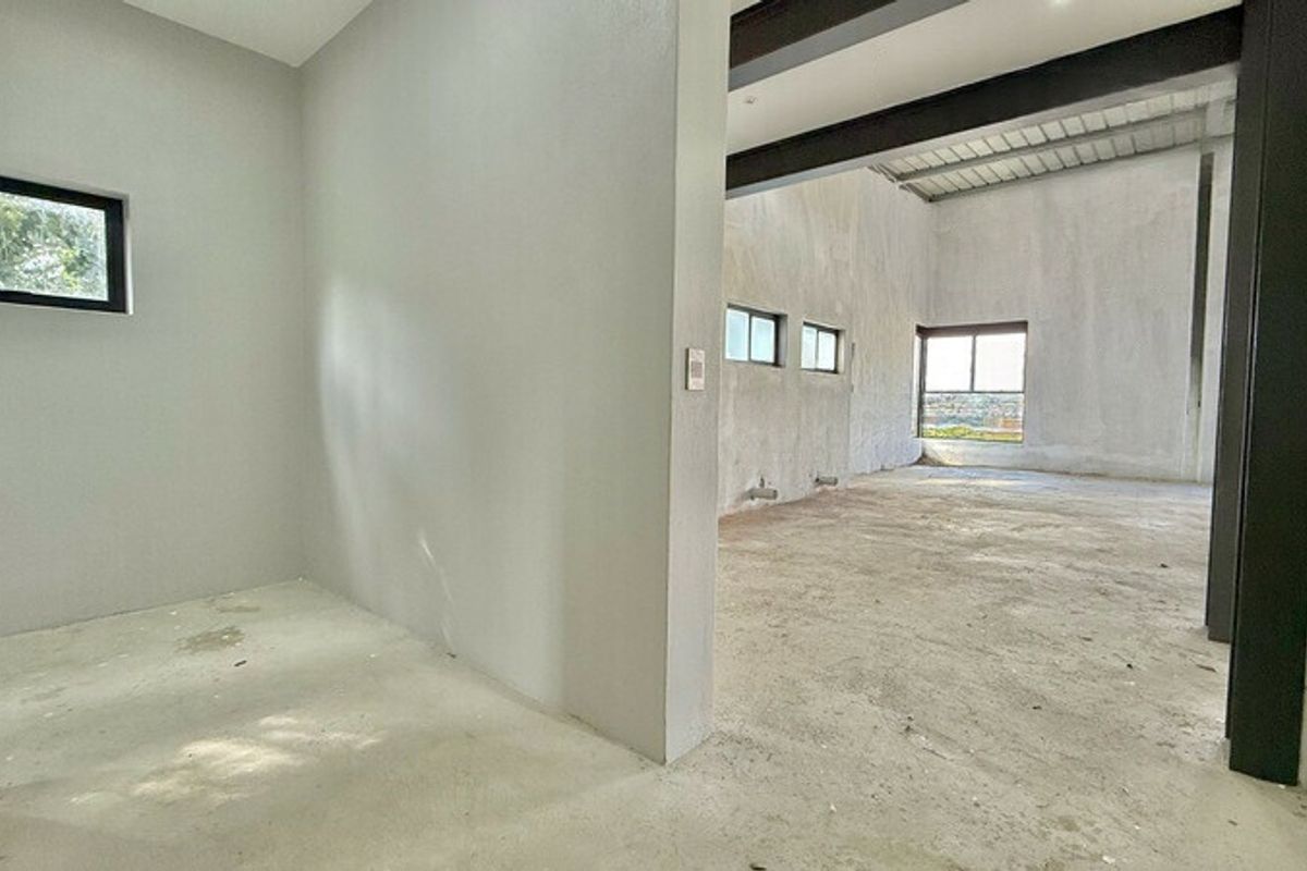 An unfinished open-plan office space featuring exposed steel beams, raw concrete flooring, and large windows providing natural light.