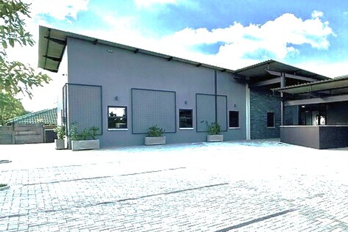 A modern office building exterior featuring a paved parking area, metal roofing, and stone cladding accents under a clear sky.