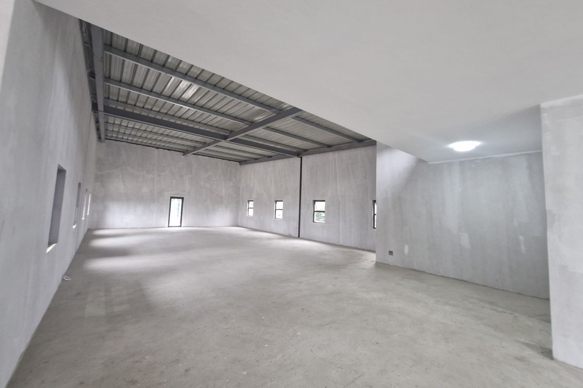 A spacious, open-plan office area featuring exposed steel roof trusses, concrete flooring, and unfinished plastered walls, offering a blank canvas for custom fit-outs.
