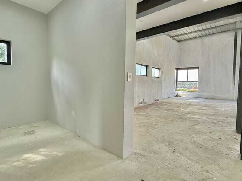An unfinished open-plan office space featuring exposed steel beams, raw concrete flooring, and large windows providing natural light.