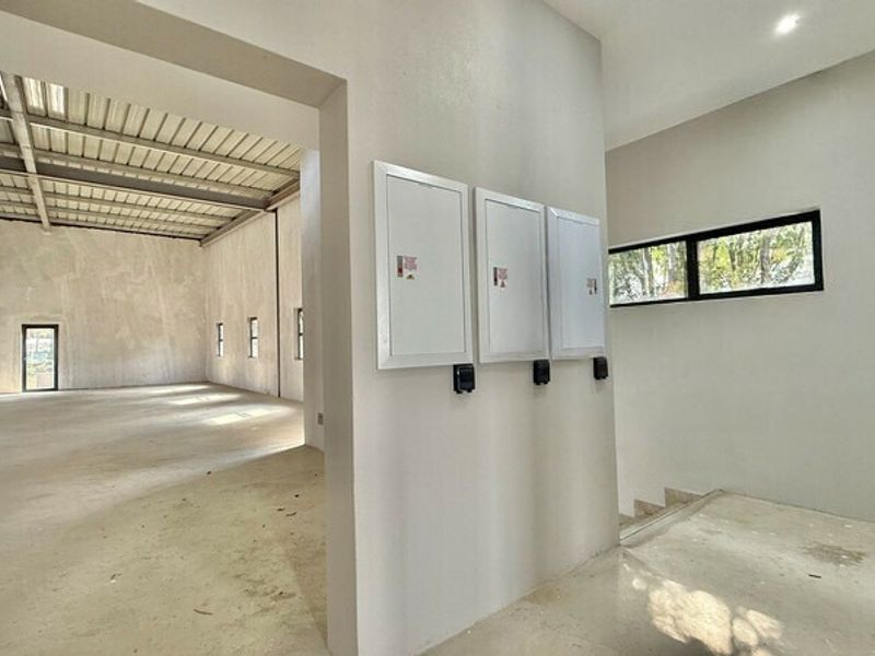 Spacious open-plan office area featuring exposed steel roof trusses, concrete flooring, and wall-mounted electrical distribution boards in a modern industrial shell.