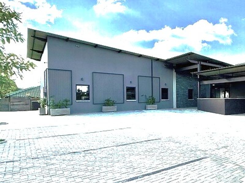 A modern office building exterior featuring a paved parking area, metal roofing, and stone cladding accents under a clear sky.