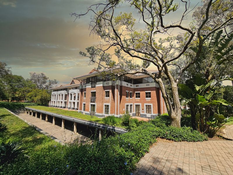 A well-maintained multi-story office building featuring a classic brick facade, tiled roof, and surrounding landscaped gardens with a paved walkway.