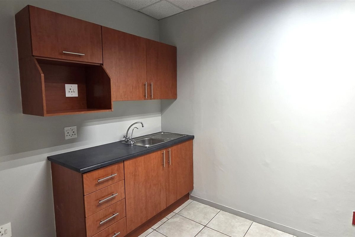 A compact office kitchenette featuring wood-finish cabinetry, a stainless steel sink, and tiled flooring, providing essential utility space for a professional environment.