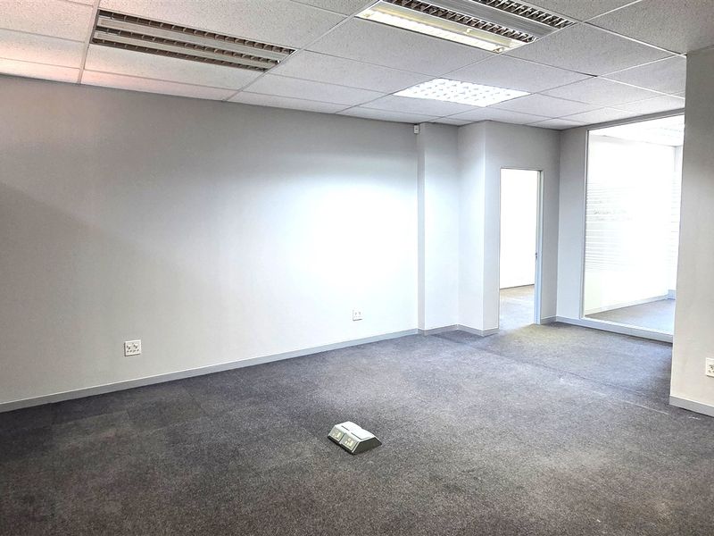 A vacant, well-lit office space featuring neutral carpeting, a suspended ceiling with recessed lighting, and glass partitions for a professional, open feel.