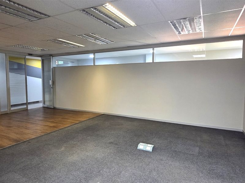 A vacant office space featuring a mix of carpet and laminate flooring, glass partitioning, and a suspended ceiling with recessed lighting.