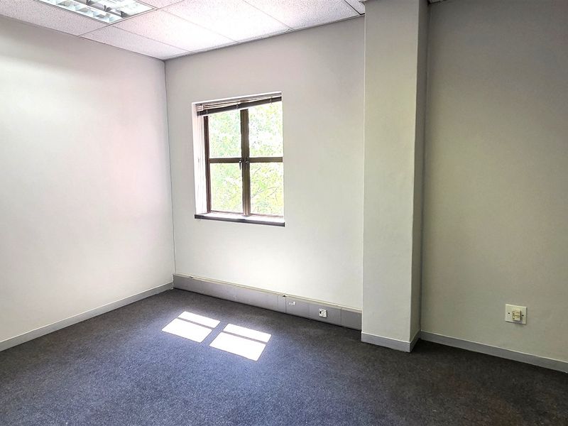 A clean, empty office space featuring neutral walls, carpet flooring, and a window providing natural light.