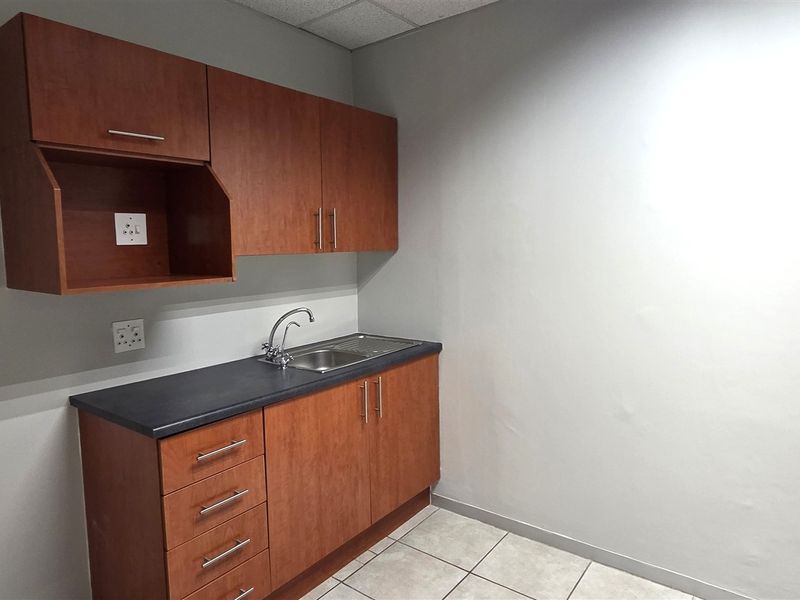 A compact office kitchenette featuring wood-finish cabinetry, a stainless steel sink, and tiled flooring, providing essential utility space for a professional environment.