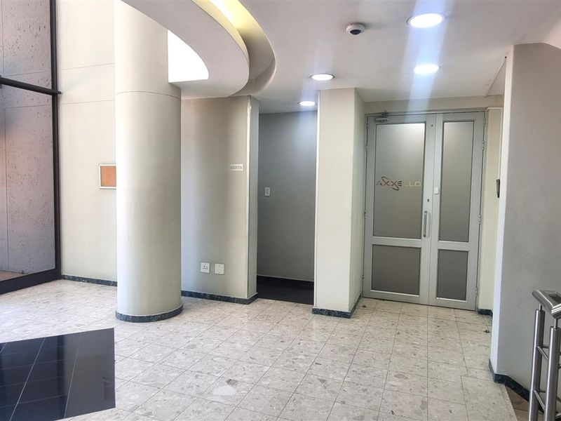 A bright and professional office building entrance featuring terrazzo flooring, recessed ceiling lighting, and double glass doors.