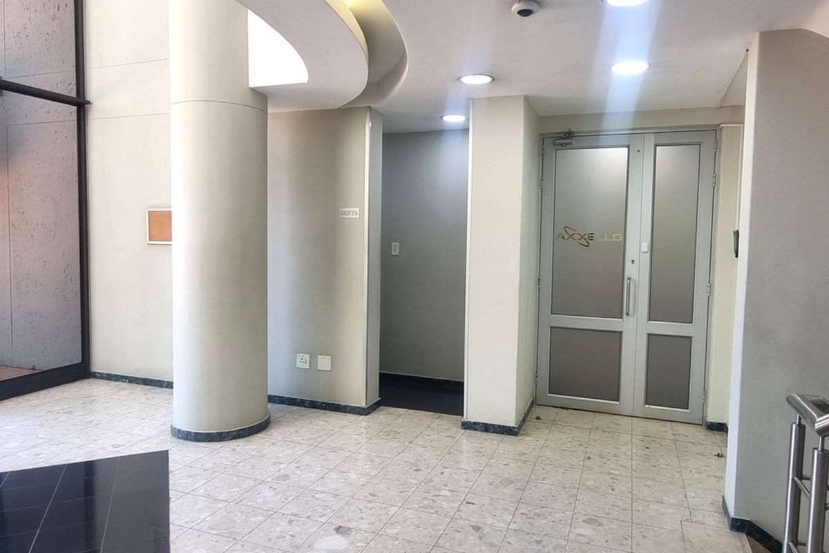 A bright and professional office building entrance featuring terrazzo flooring, recessed ceiling lighting, and double glass doors.