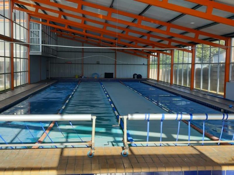 Indoor commercial swimming pool facility featuring a large lap pool, extensive glass paneling, and a high-clearance steel truss roof structure.