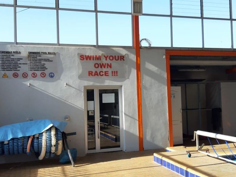 Indoor swimming pool facility featuring large windows, tiled flooring, and designated changing area access with safety signage.