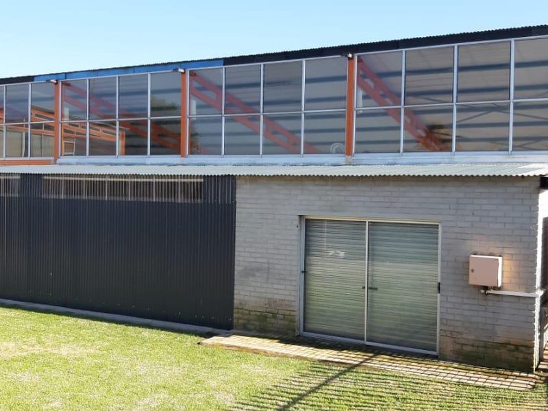 Exterior view of a commercial building featuring a combination of brick and corrugated metal cladding with large upper-level windows and an adjacent lawn area.
