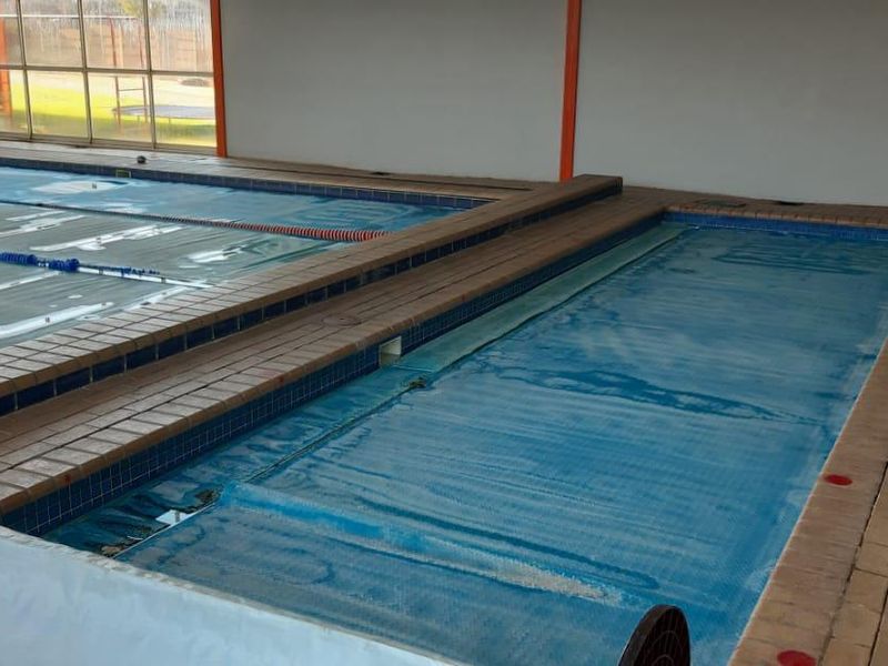 Indoor commercial swimming pool facility featuring multiple lanes, tiled surrounds, and large windows providing natural light.