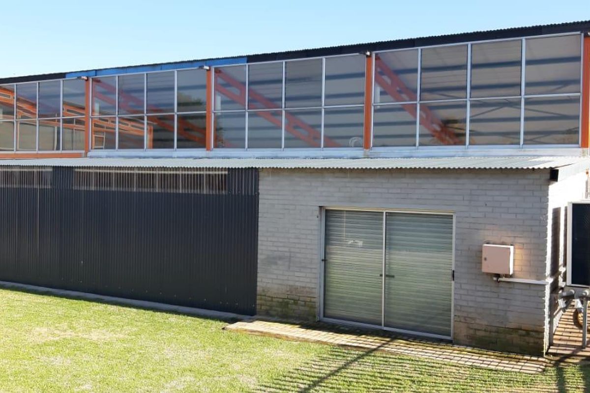 Exterior view of a commercial building featuring a combination of brick and corrugated metal cladding with large upper-level windows and an adjacent lawn area.