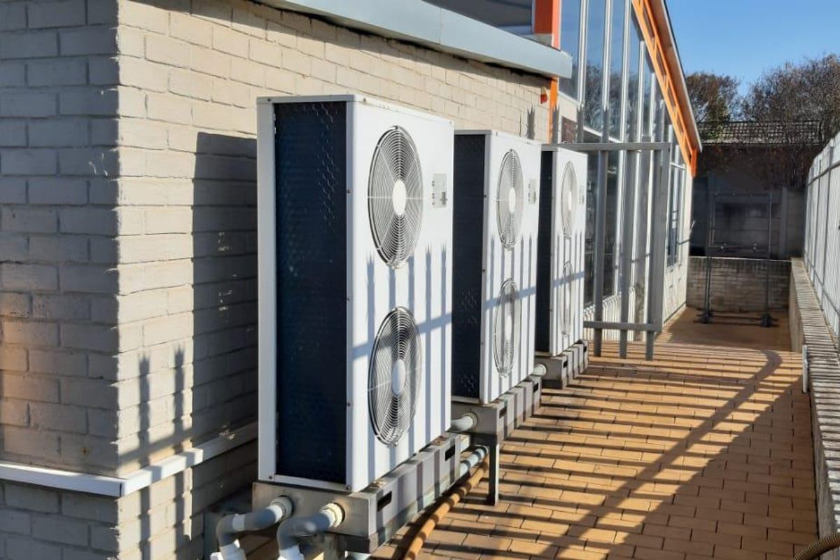 Exterior side area featuring a row of industrial HVAC condenser units mounted on a paved walkway alongside the building facade.