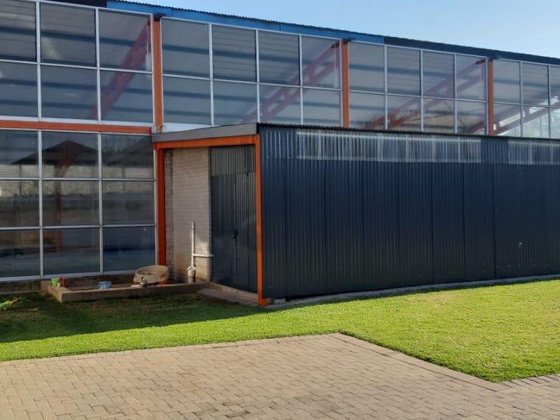 Rear view of a commercial building featuring large glass panel windows, a corrugated metal extension, and a paved courtyard area with lawn.