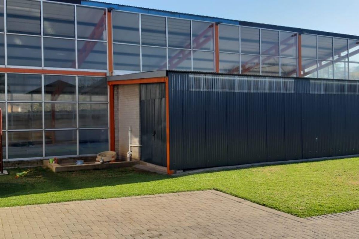 Rear view of a commercial building featuring large glass panel windows, a corrugated metal extension, and a paved courtyard area with lawn.