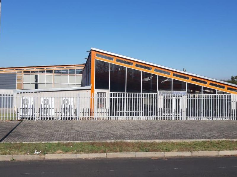 Modern commercial building featuring a distinctive mono-pitch roof, extensive glass facade, and secure perimeter fencing, situated along a paved street.