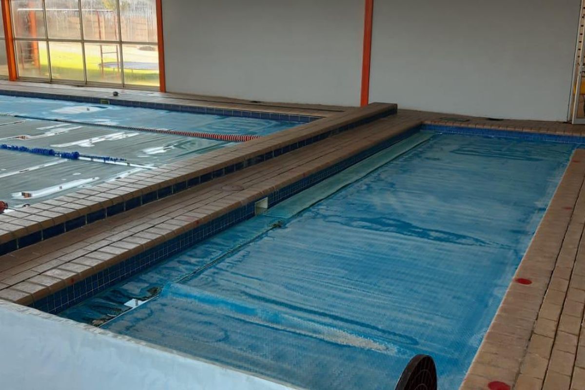 Indoor commercial swimming pool facility featuring multiple lanes, tiled surrounds, and large windows providing natural light.