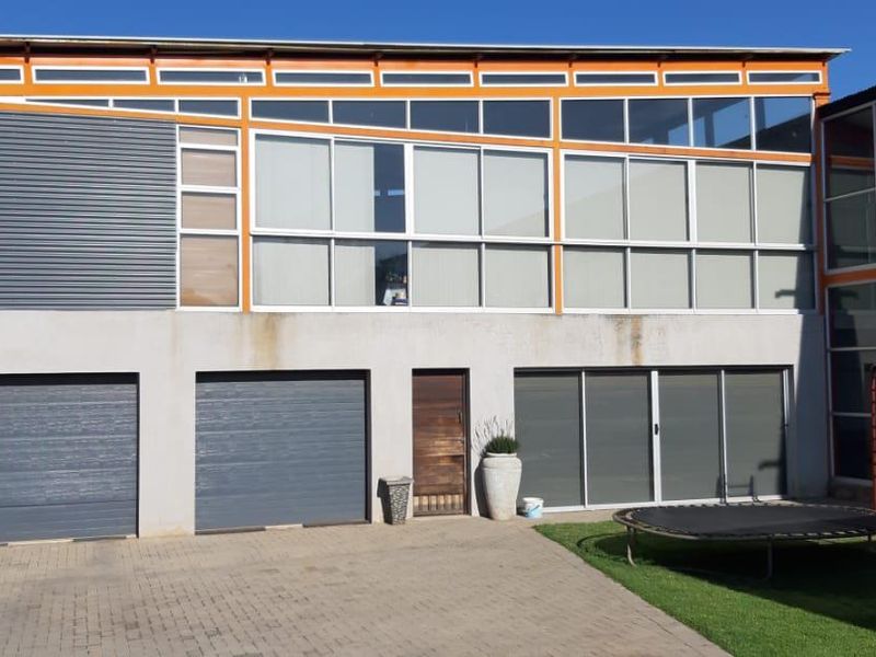 Rear exterior view of a commercial building featuring multiple garage doors, large glass windows, and a paved driveway area.