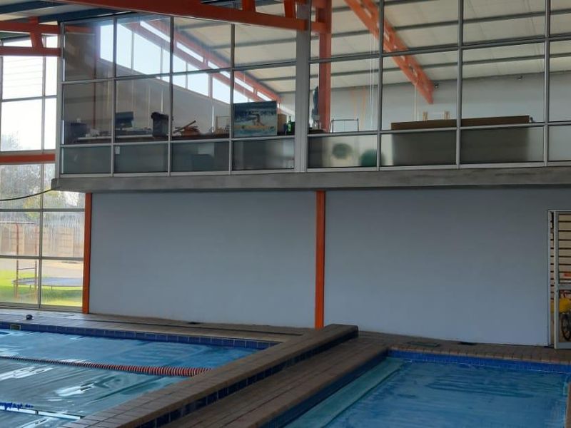 Indoor swimming pool facility featuring a large lap pool, tiled surround, and an elevated mezzanine level with glass partitioning.