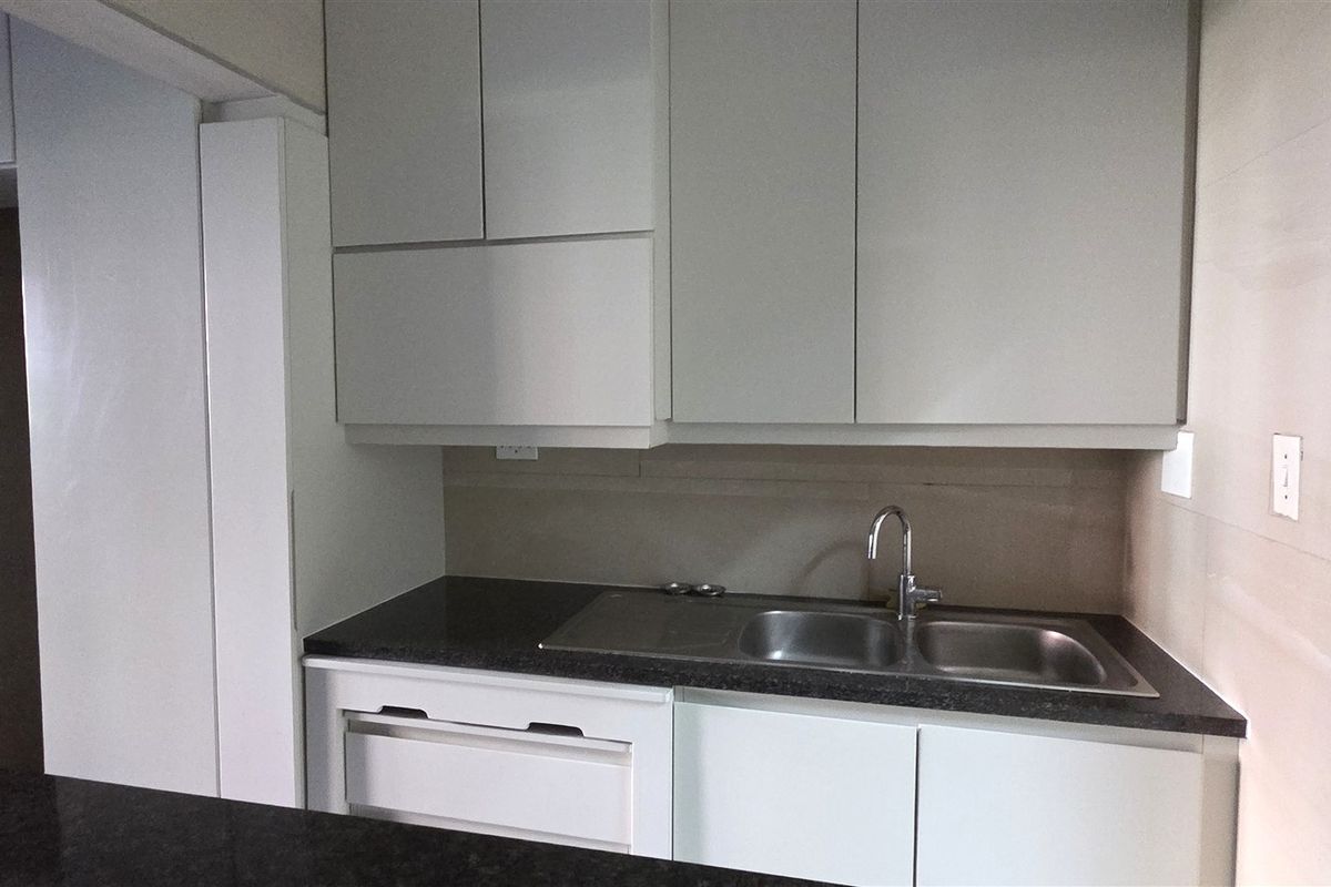 A clean, modern kitchen area featuring white built-in cabinetry, a dark stone countertop, and a double bowl stainless steel sink.