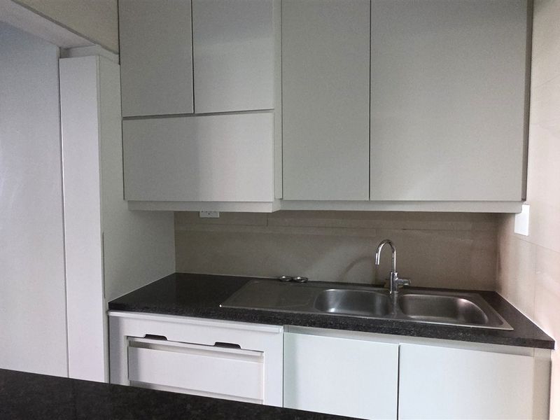 A clean, modern kitchen area featuring white built-in cabinetry, a dark stone countertop, and a double bowl stainless steel sink.