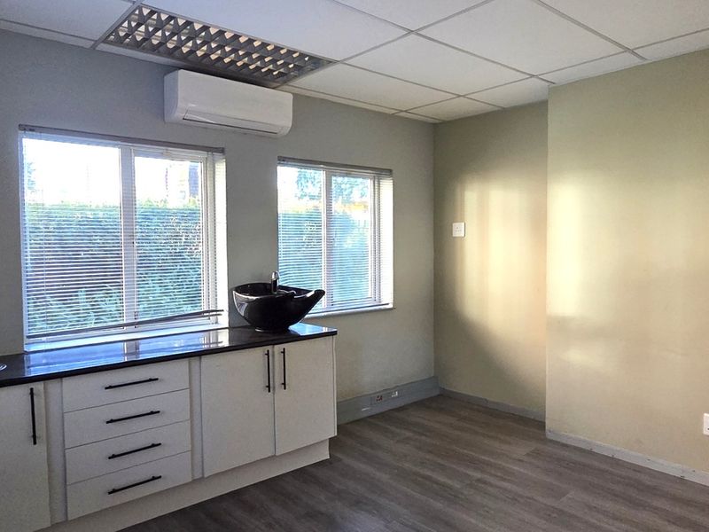 A clean, empty office space featuring built-in cabinetry with a basin, modern laminate flooring, and an integrated air conditioning unit.