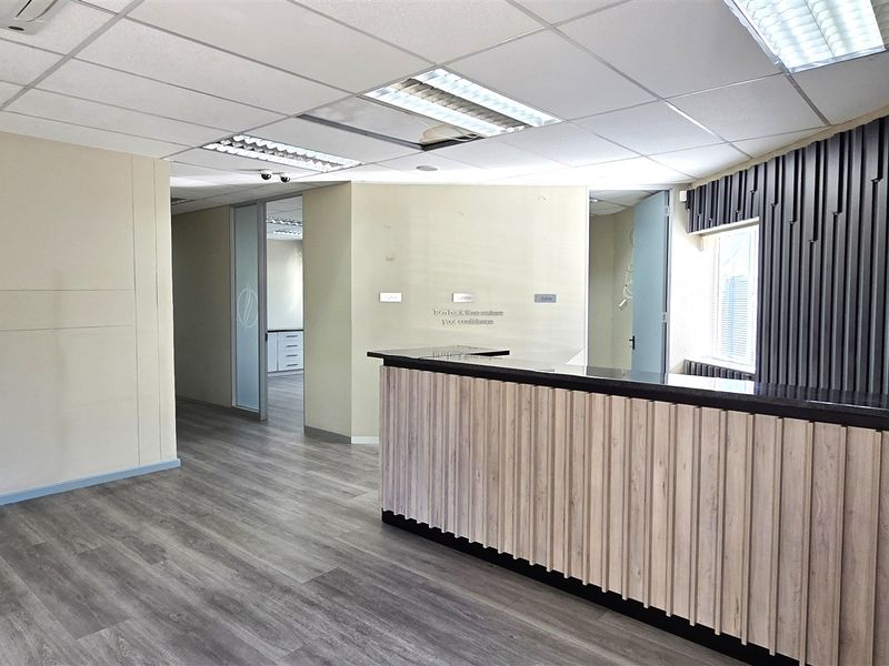 A professional office reception area featuring a modern built-in desk, wood-look laminate flooring, suspended ceiling, and decorative vertical slat wall paneling.