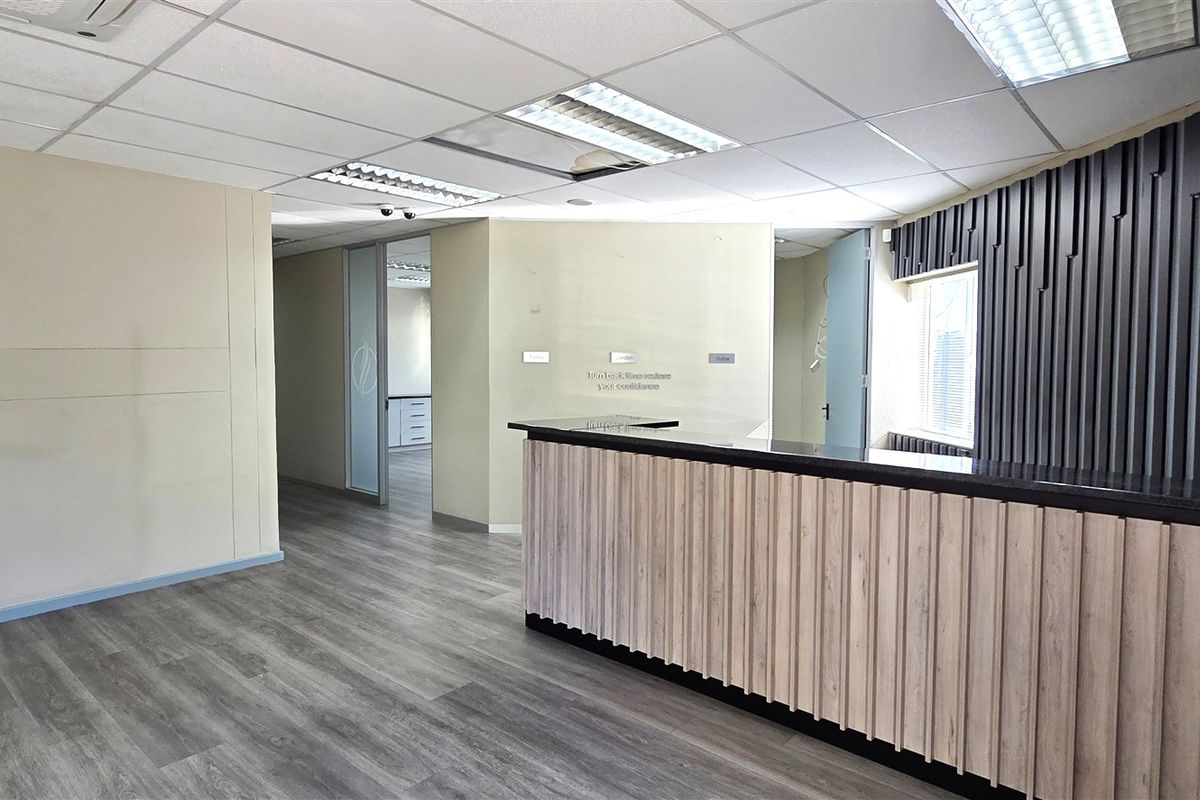 A professional office reception area featuring a modern built-in desk, wood-look laminate flooring, suspended ceiling, and decorative vertical slat wall paneling.