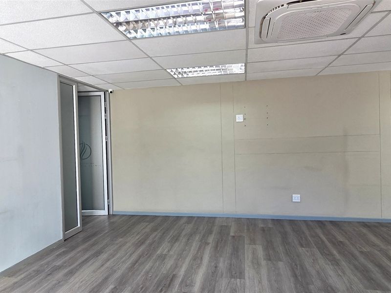 An empty office space featuring laminate flooring, a suspended ceiling with recessed lighting, and a ceiling-mounted air conditioning unit.