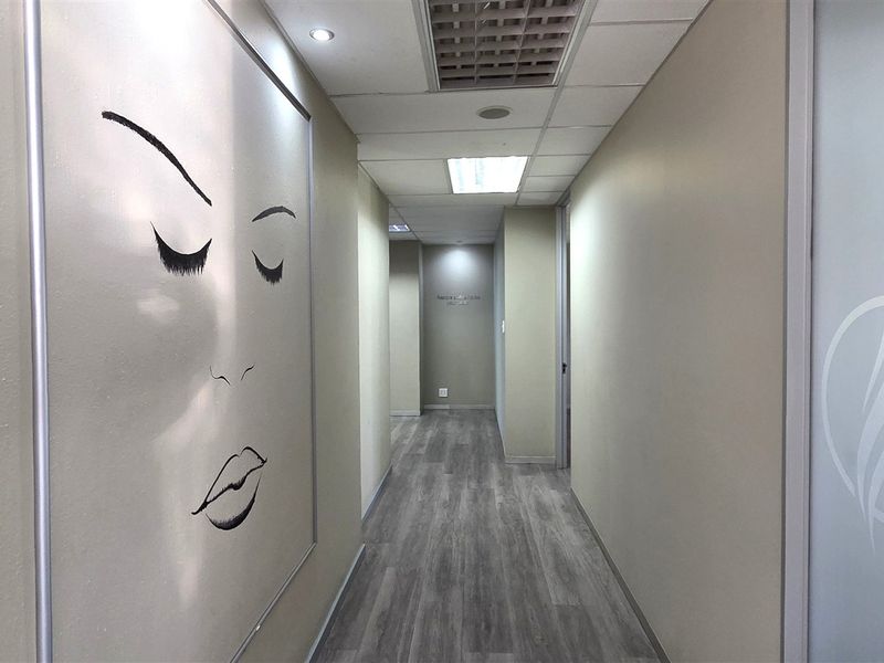 A clean, modern office hallway featuring laminate wood flooring, recessed ceiling lighting, and a frosted glass door leading to an adjacent workspace.