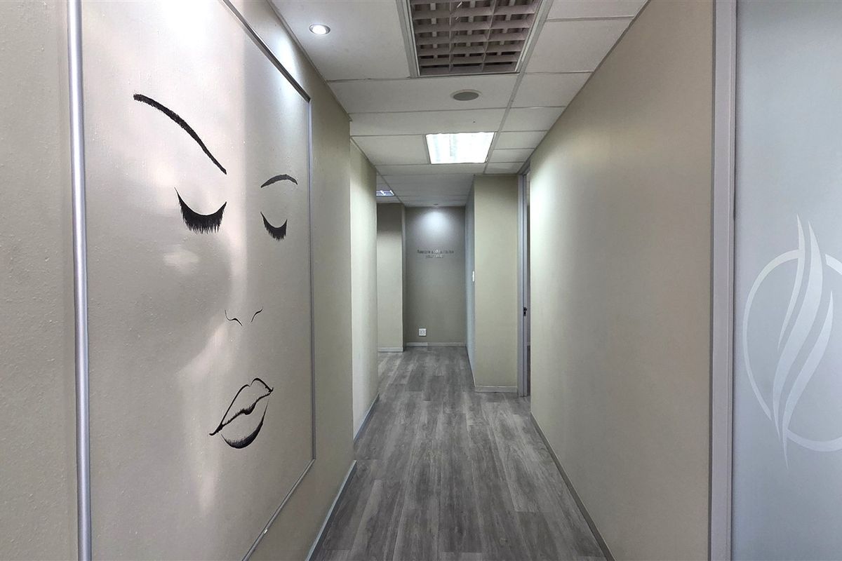A clean, modern office hallway featuring laminate wood flooring, recessed ceiling lighting, and a frosted glass door leading to an adjacent workspace.