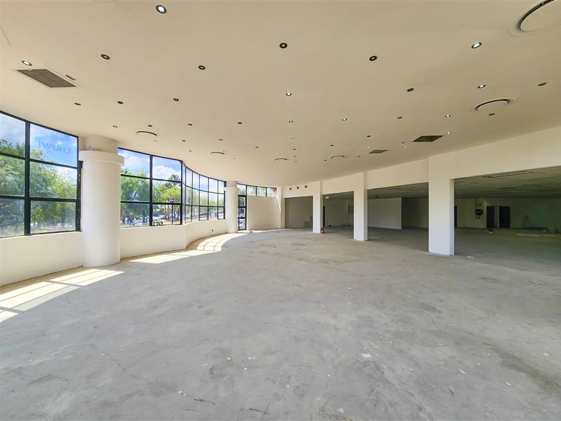 Spacious open-plan office area featuring large curved windows, recessed lighting, and structural columns, currently in a shell condition ready for custom fit-out.