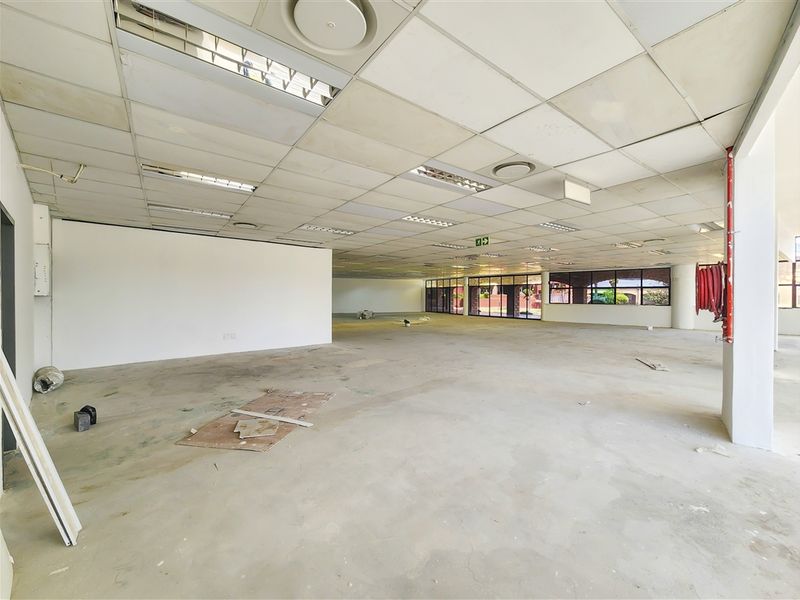 A large, open-plan office space featuring a suspended ceiling, recessed lighting, and expansive windows, currently in a vacant, shell-like condition.