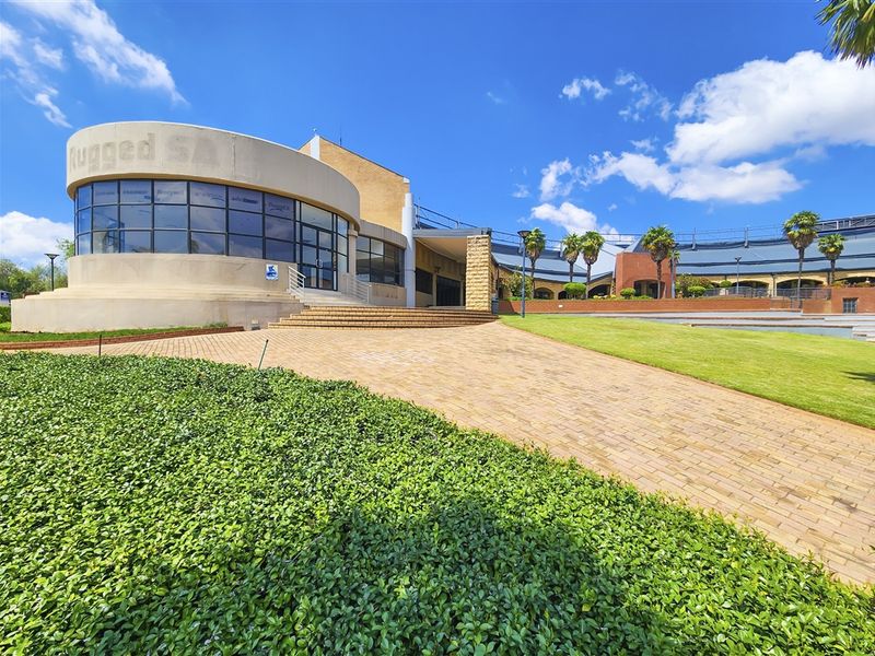 A modern office building exterior featuring a prominent curved glass facade, paved entrance area, and well-maintained landscaped grounds.