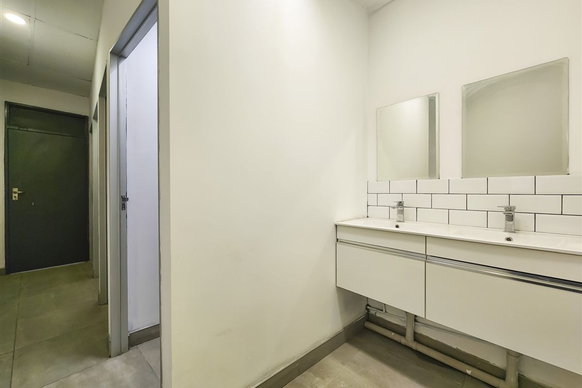 A functional office bathroom featuring a double vanity with subway tile backsplash, wall-mounted mirrors, and tiled flooring.