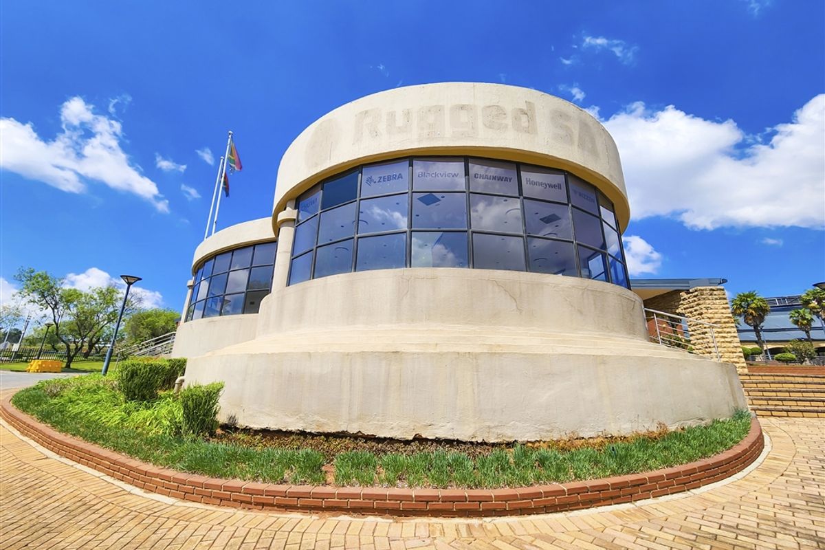 Exterior view of a modern office building featuring a distinctive curved concrete facade, large glass windows, and a paved entrance area.
