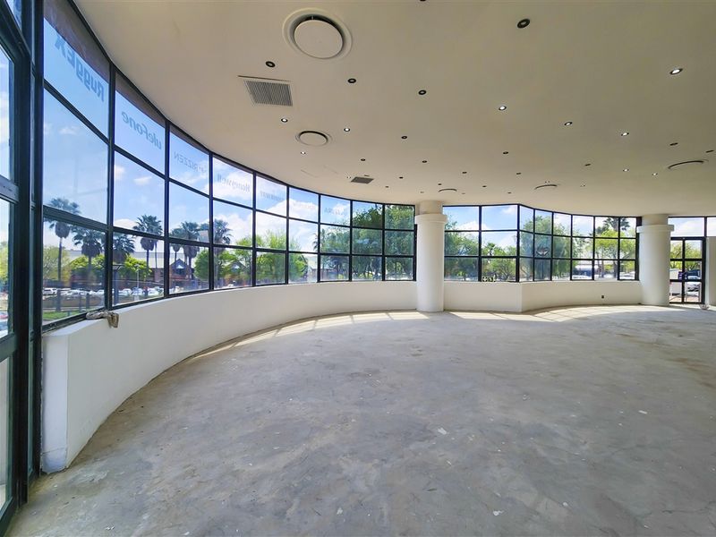 Spacious, open-plan office area featuring expansive curved windows, recessed lighting, and central air conditioning, currently awaiting final flooring installation.