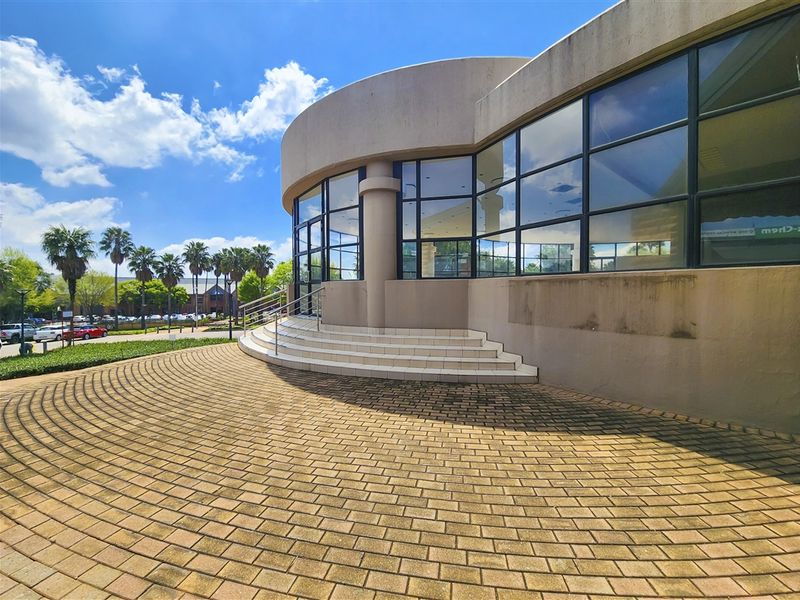 Exterior view of a modern office building featuring a curved facade, large glass windows, and a paved entrance area with tiled steps.