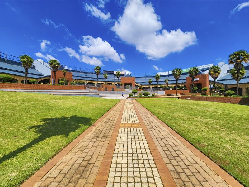 A wide-angle view of a commercial office complex featuring a central paved walkway, manicured lawns, and brick-accented building facades under a clear sky.
