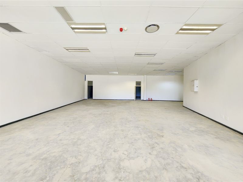 A spacious, open-plan office area featuring a suspended ceiling with recessed lighting, air conditioning, and unfinished concrete flooring.