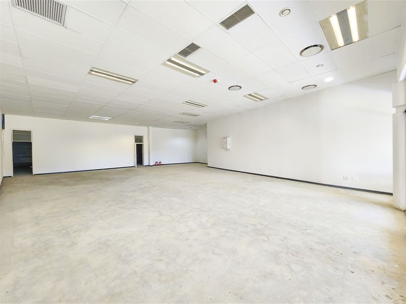 A spacious, open-plan office area featuring a suspended ceiling with integrated lighting, air conditioning vents, and unfinished concrete flooring.