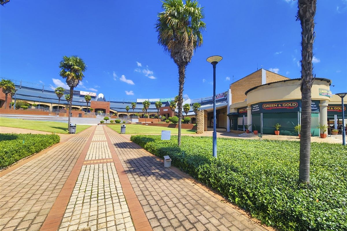 A well-maintained outdoor commercial plaza featuring paved walkways, landscaped gardens with palm trees, and access to various office and retail storefronts.