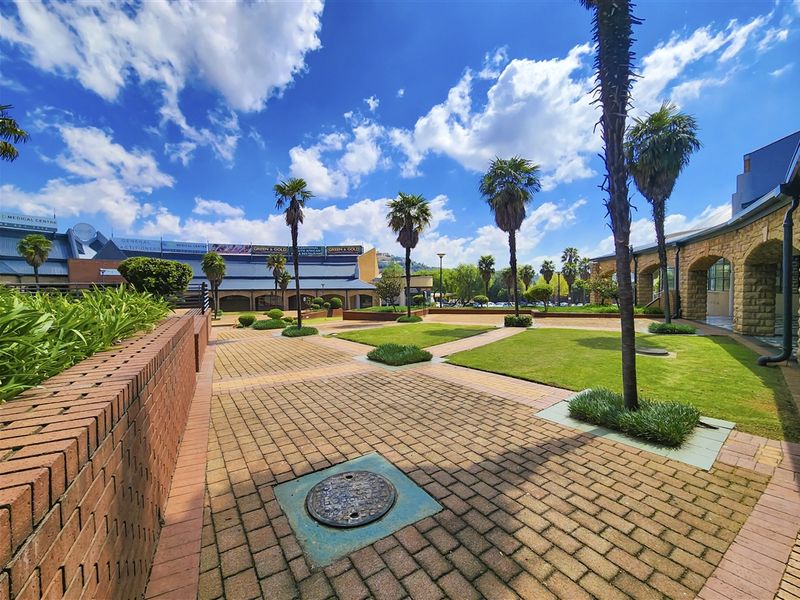 A well-maintained outdoor courtyard area featuring brick paving, manicured lawn sections, and established palm trees within an office park setting.