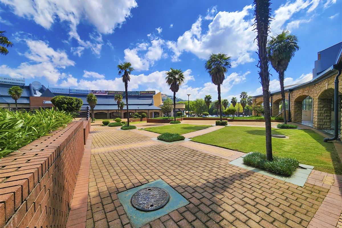 A well-maintained outdoor courtyard area featuring brick paving, manicured lawn sections, and established palm trees within an office park setting.