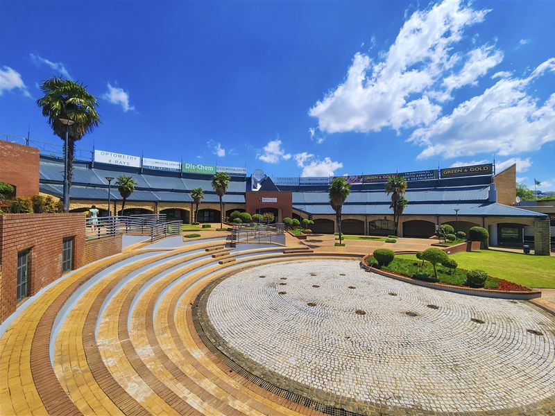 A well-maintained commercial office complex courtyard featuring tiered brick paving, landscaped garden beds, and prominent signage for various medical and retail tenants.