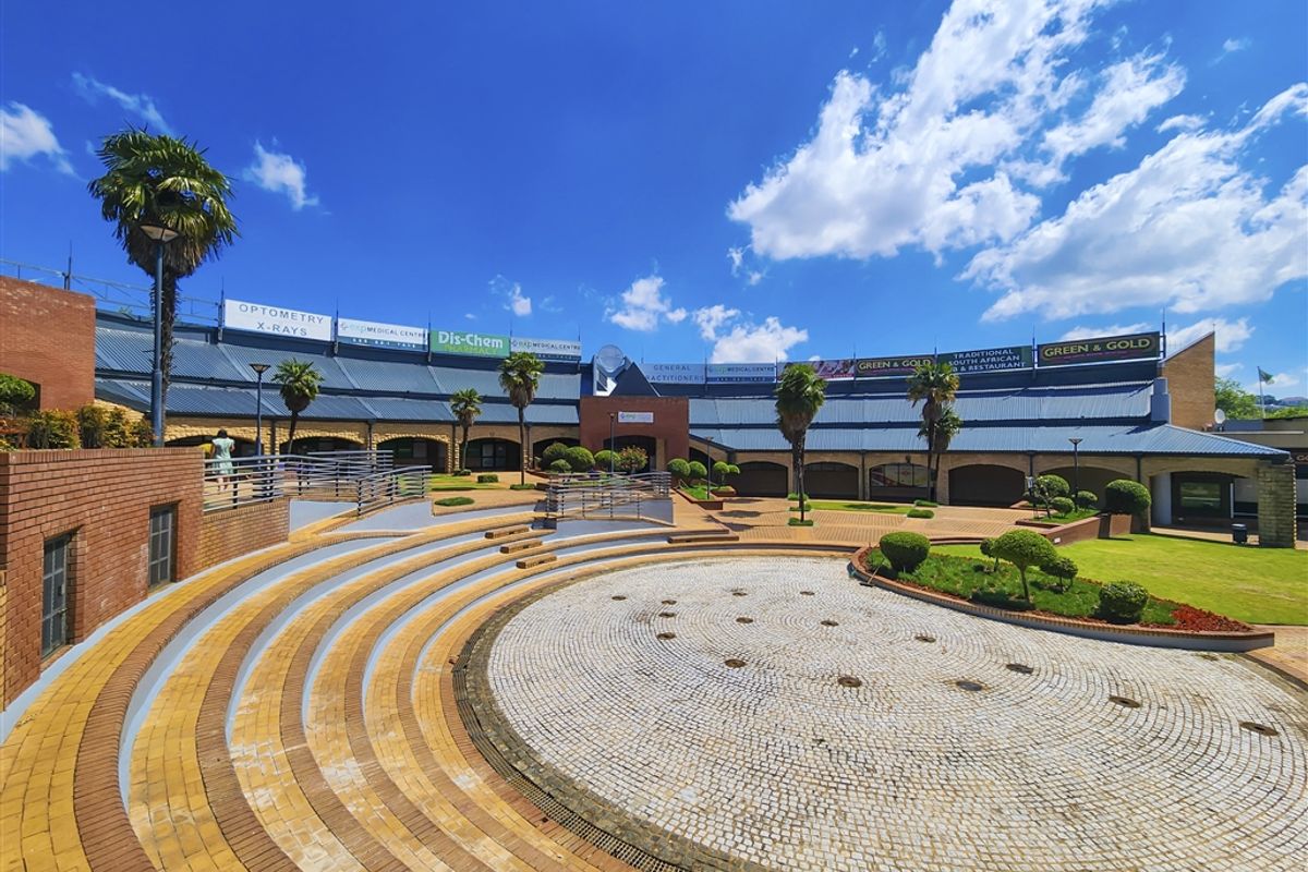 A well-maintained commercial office complex courtyard featuring tiered brick paving, landscaped garden beds, and prominent signage for various medical and retail tenants.