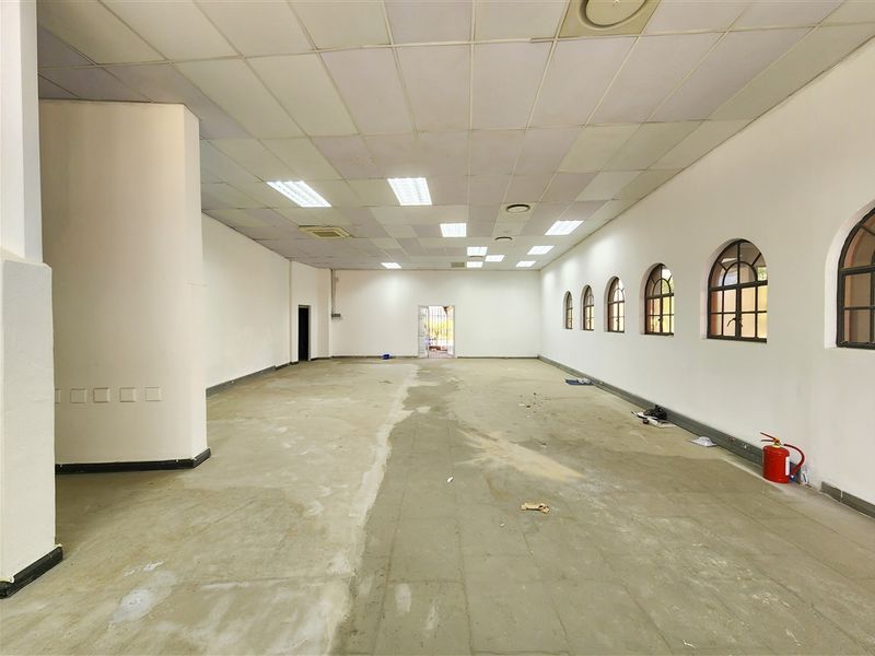 A spacious, empty office area featuring a suspended ceiling, recessed lighting, and multiple arched windows, ready for customization.